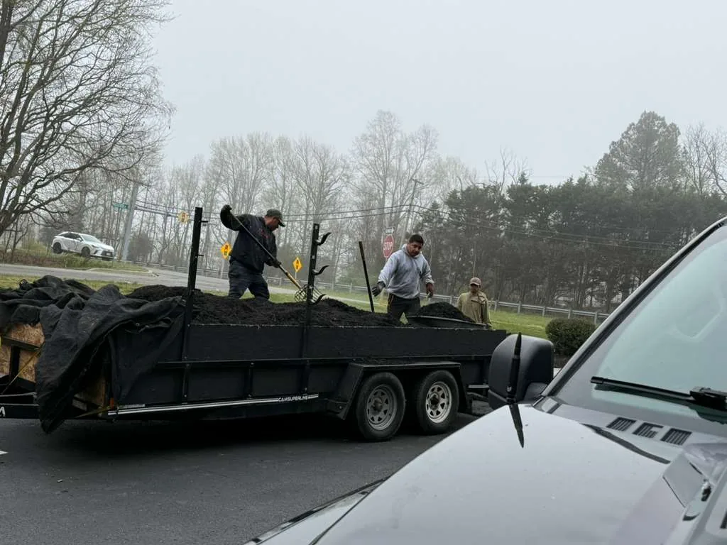 Crew unloading mulch from a loaded trailer at a property